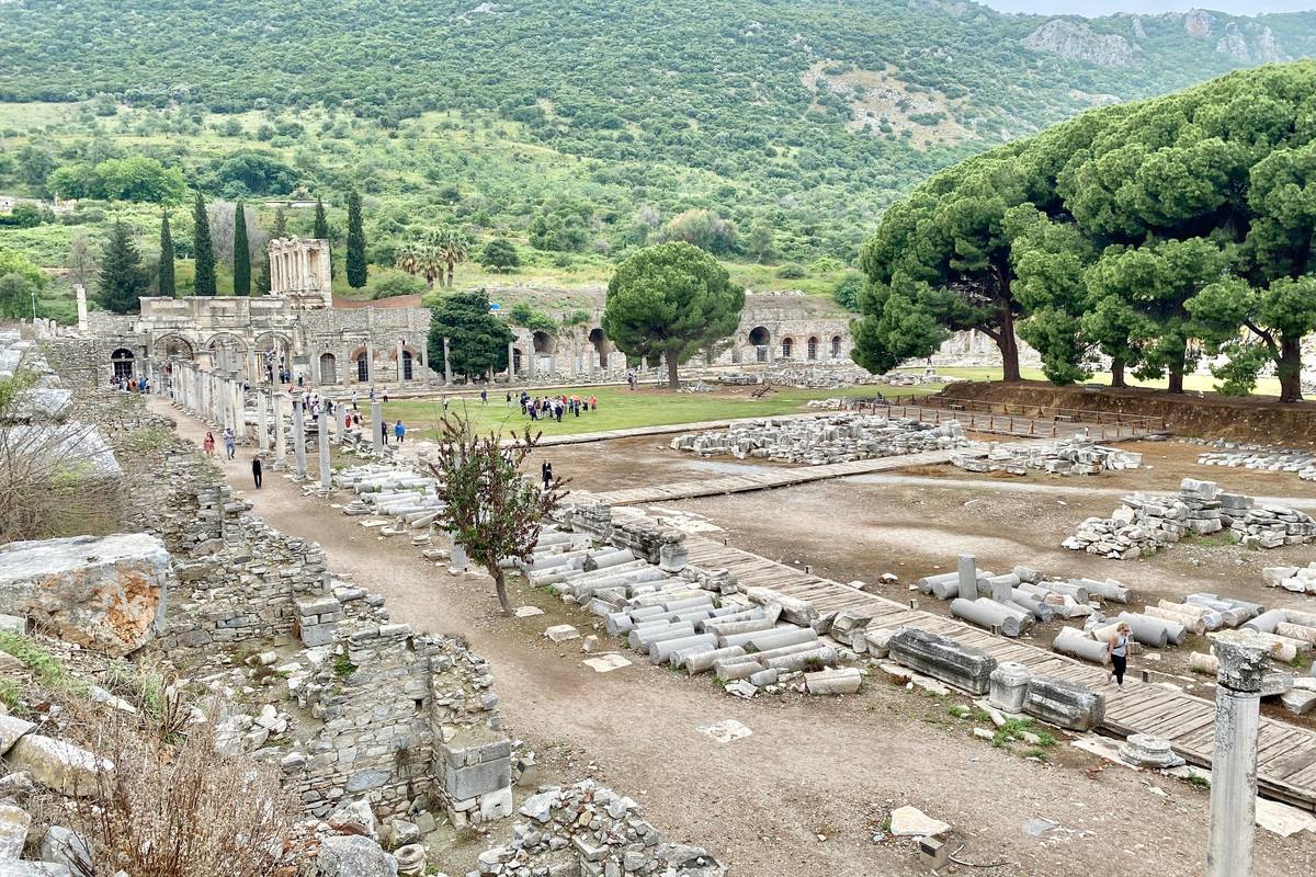 El ágora comercial de Éfeso vista desde lo alto: una gran explanada con tambores de columna caídos y pasarelas de madera, y la Biblioteca de Celso al fondo a la izquierda