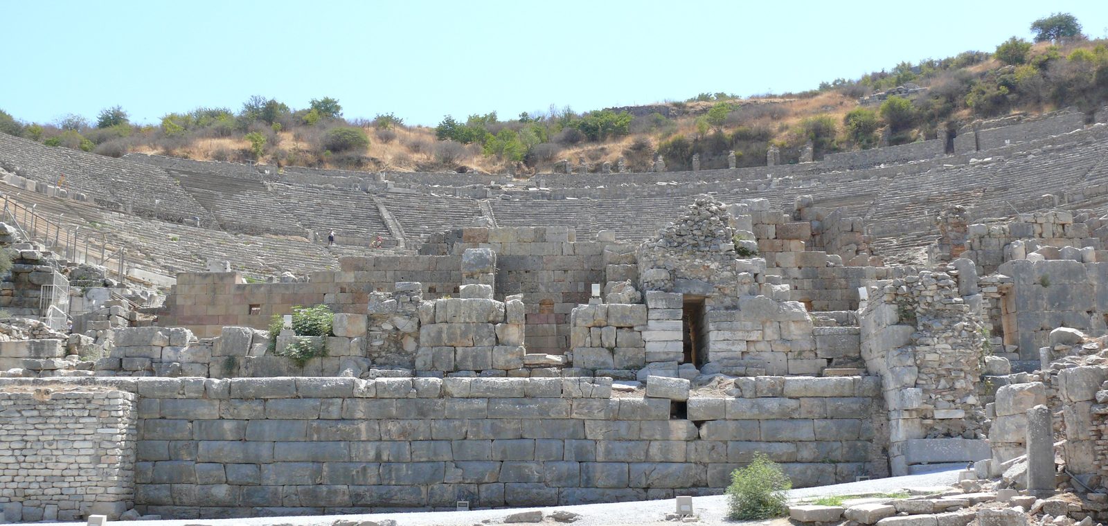 El Gran Teatro de Éfeso visto desde abajo: los muros de piedra del edificio de la escena en primer plano y, detrás, las gradas en semicírculo subiendo por la ladera bajo un cielo azul